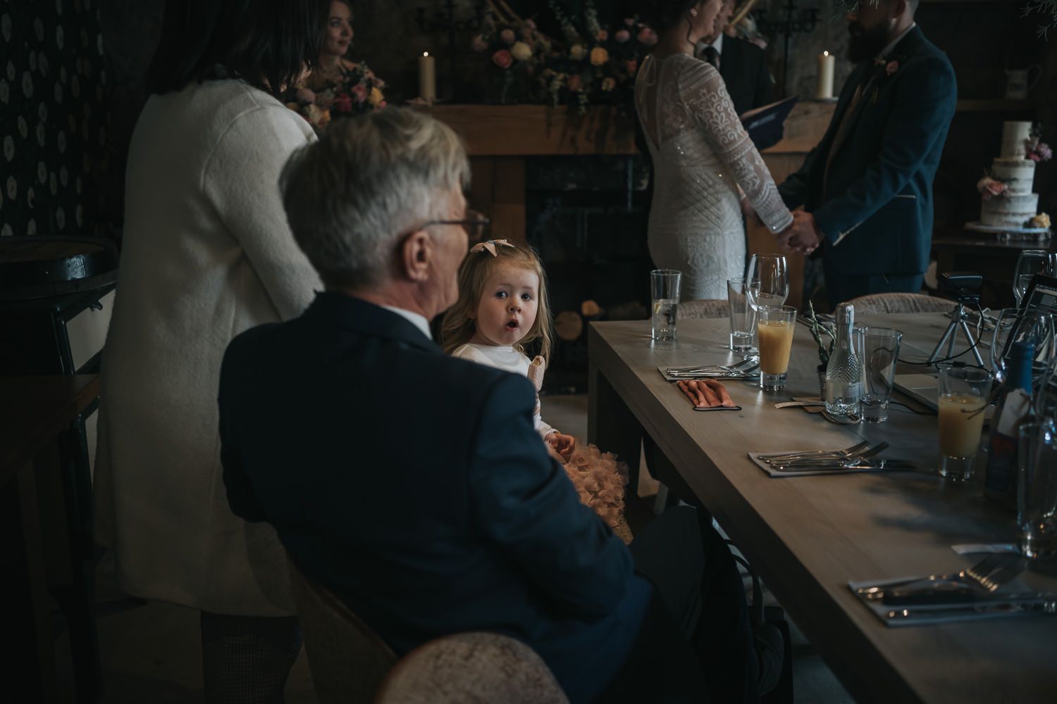 A small child smiles at the camera as the couple get married in the background