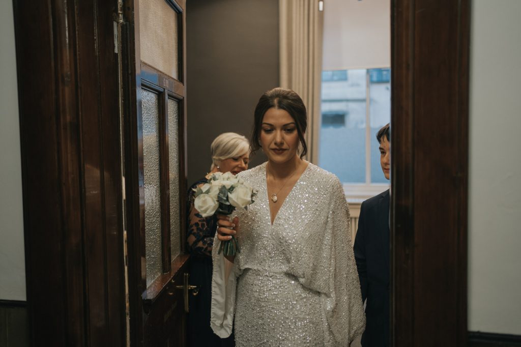 The bride holds her younger brothers hand as they walk out the door to the ceremony room