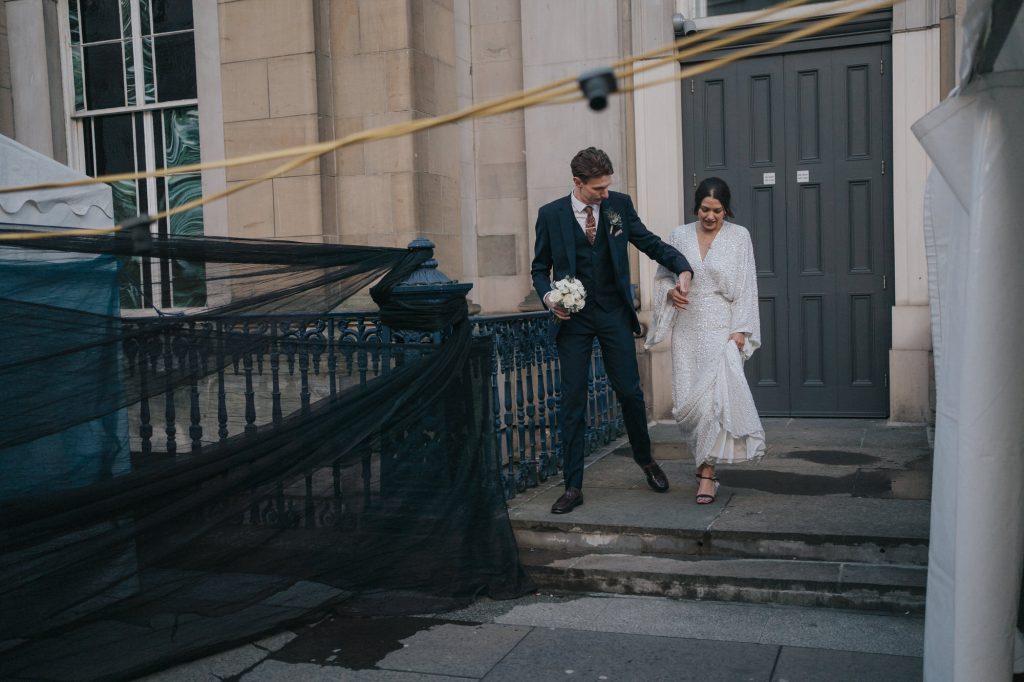 The bride and groom hold hands as thy walk through the streets of Glasgow