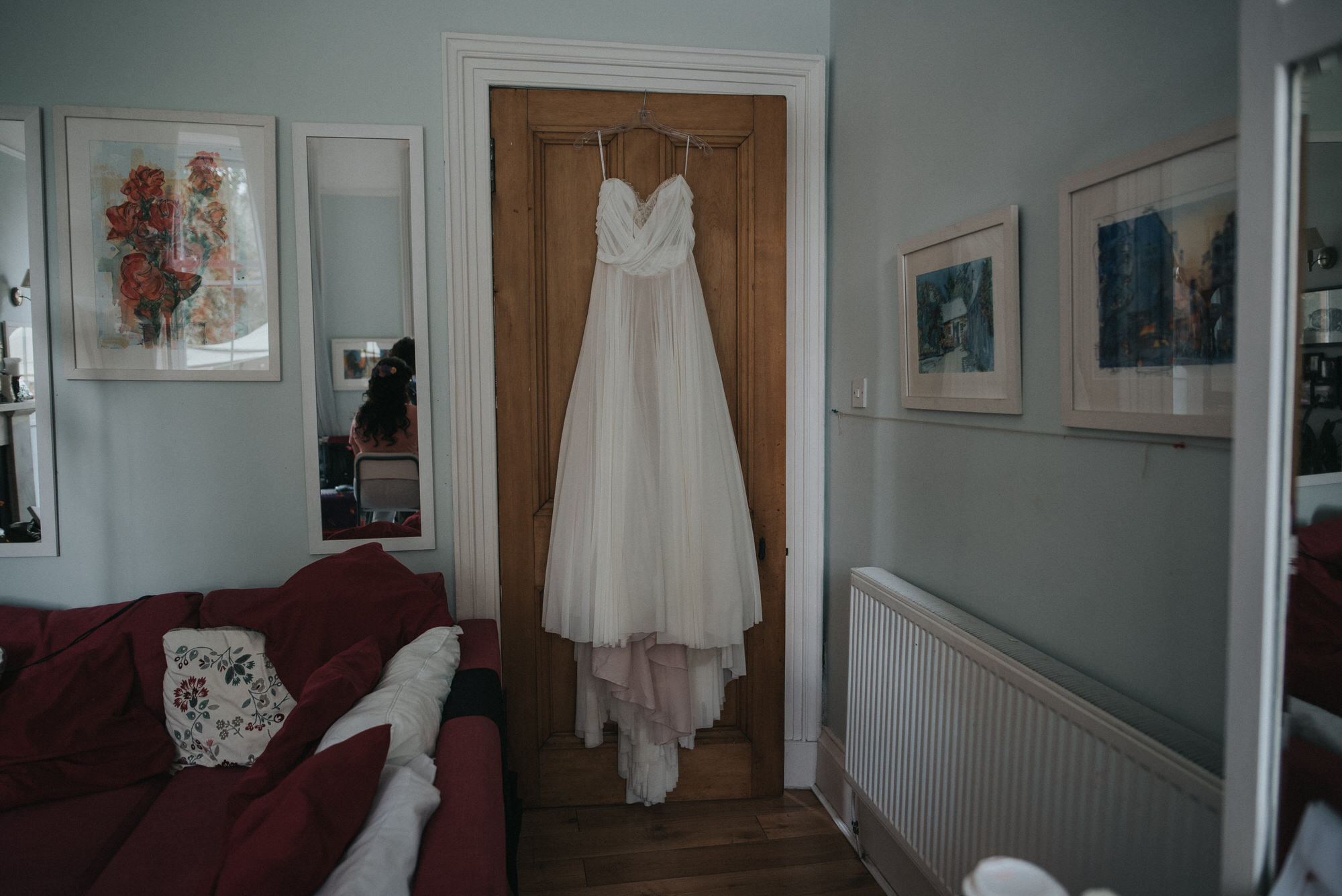 The brides wedding dress hangs over. a door. in her living room