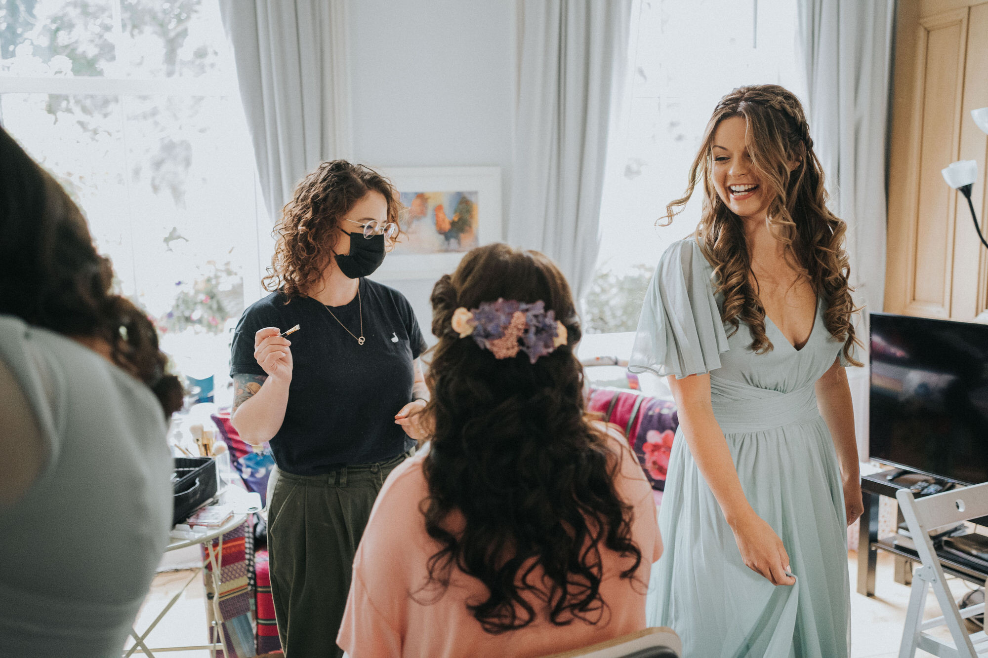 A bridesmaids laughs with the bride as she has her make up done