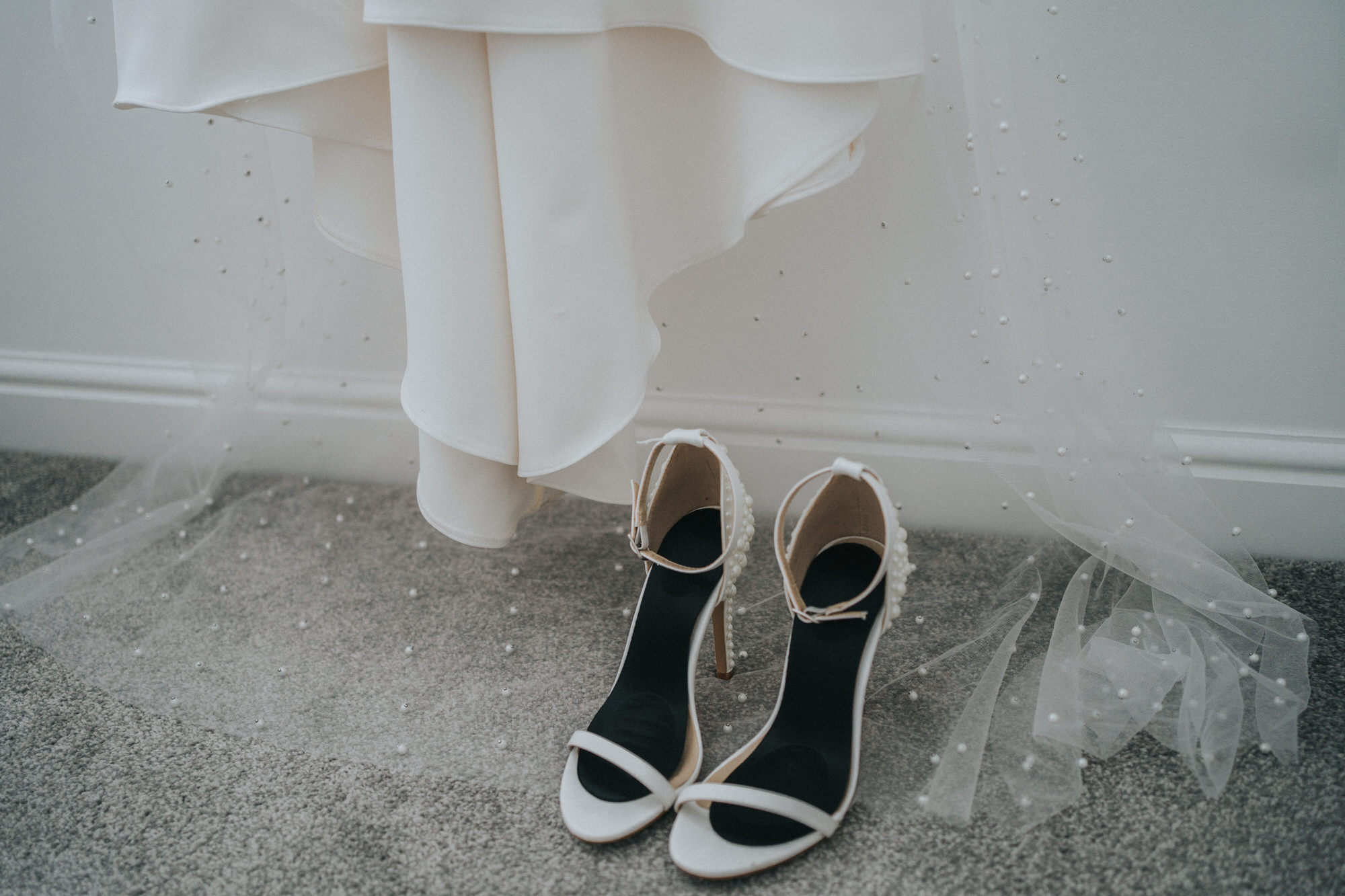 A pair of wedding shoes sit underneath a wedding dress