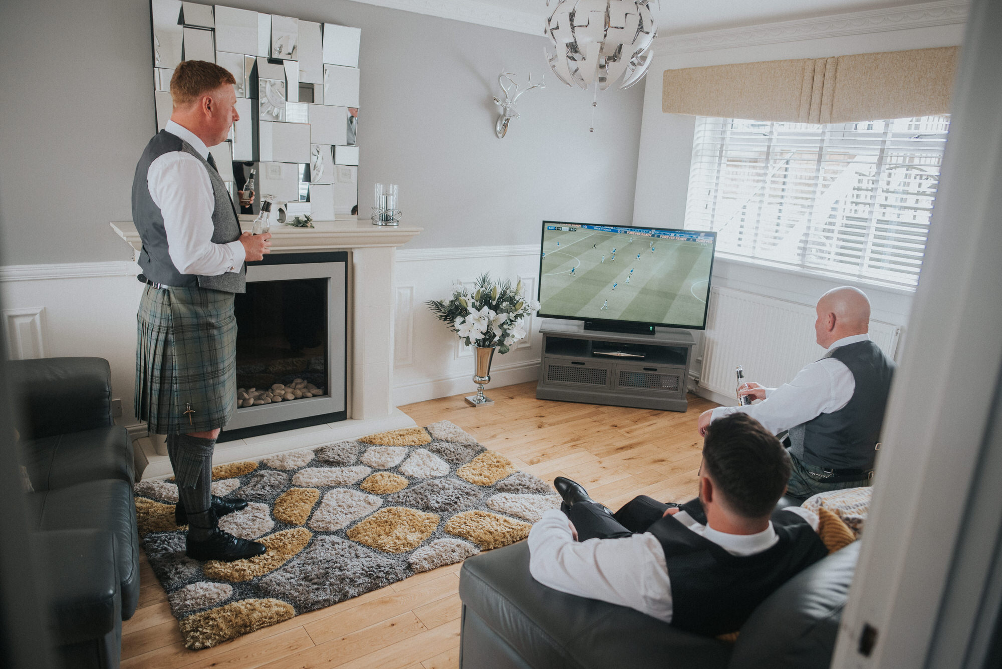 A groom sits in his living room watching the football with his family