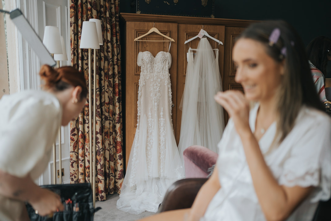 An out of focus bride laughs - we can see her wedding dress and veil behind her