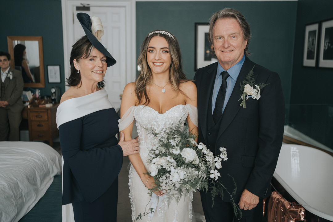 A formal shot of bride along with her Mum and Dad smiles just before they leave for the ceremony