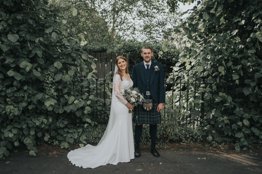 A bride and groom stand amongst some greenery at hotel du vin in Glasgow