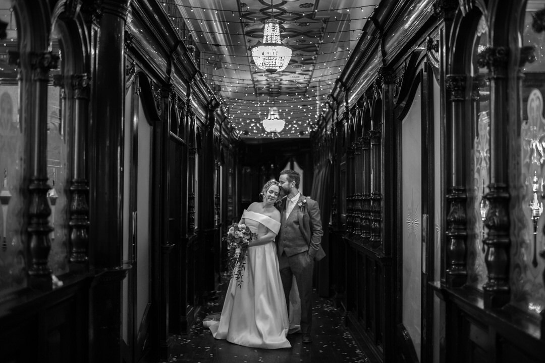 A black and white photo of a married couple inside Sloans in Glasgow, they are surrounded by a dark wooden bar