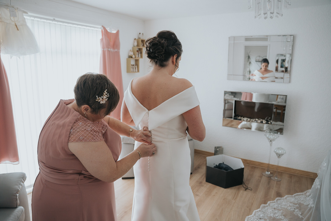 A photograph of the back of the bride as her maid of honour fixes her dress