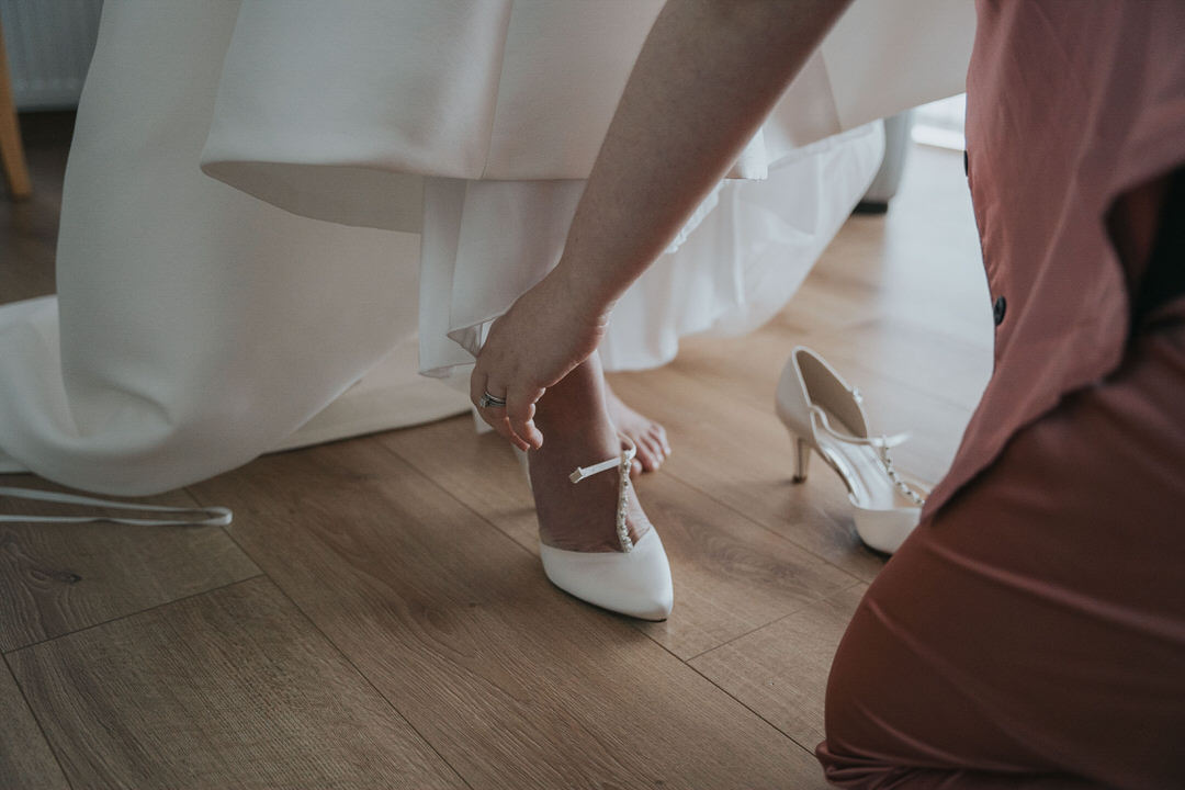 The bride slides her foot into her white wedding heels