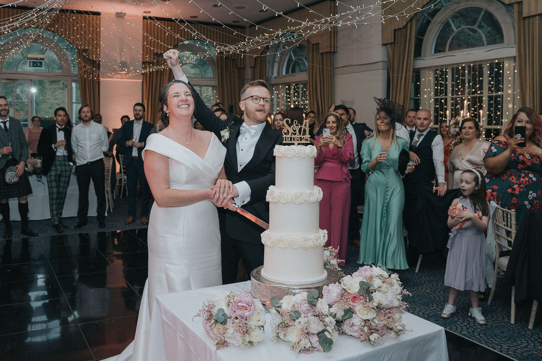 The bride and groom cheer as they cut their cake at Balbirnie house Hotel 