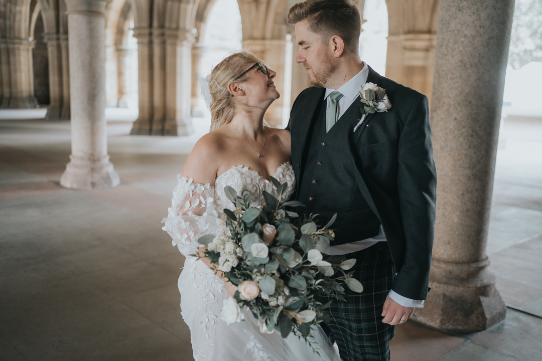 A Bride and Groom look at each other in the cloisters of Glasgow University
