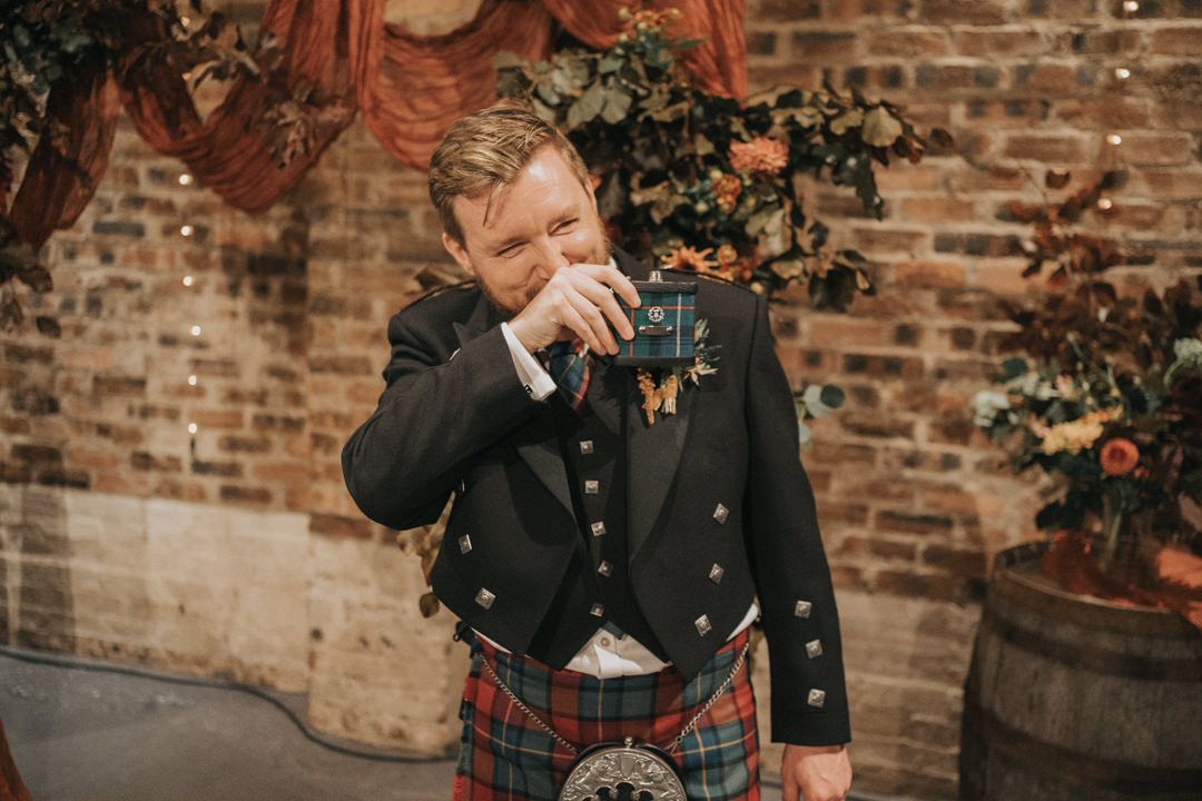 The groom laughs as he takes a drink from his hip flask at a Kinkell Byre Wedding in September