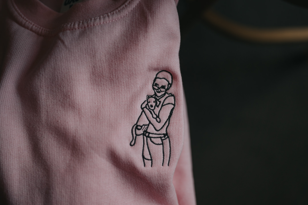 The bride has a pink jumper that has an embroidered photo of her and her dog