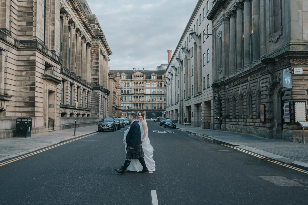 A bride and groom walk across a road in glasgow